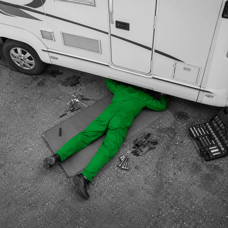 Mechanik leży pod kamperem i go naprawia zachowując bezpieczeństwo i BHP.